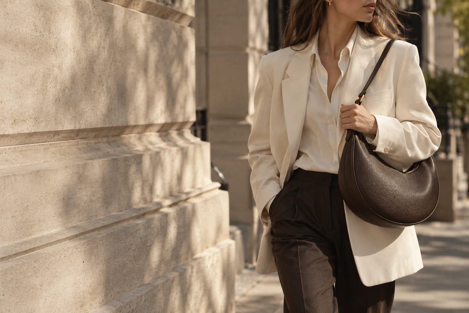 An ivory jacket paired with a chocolate crescent bag